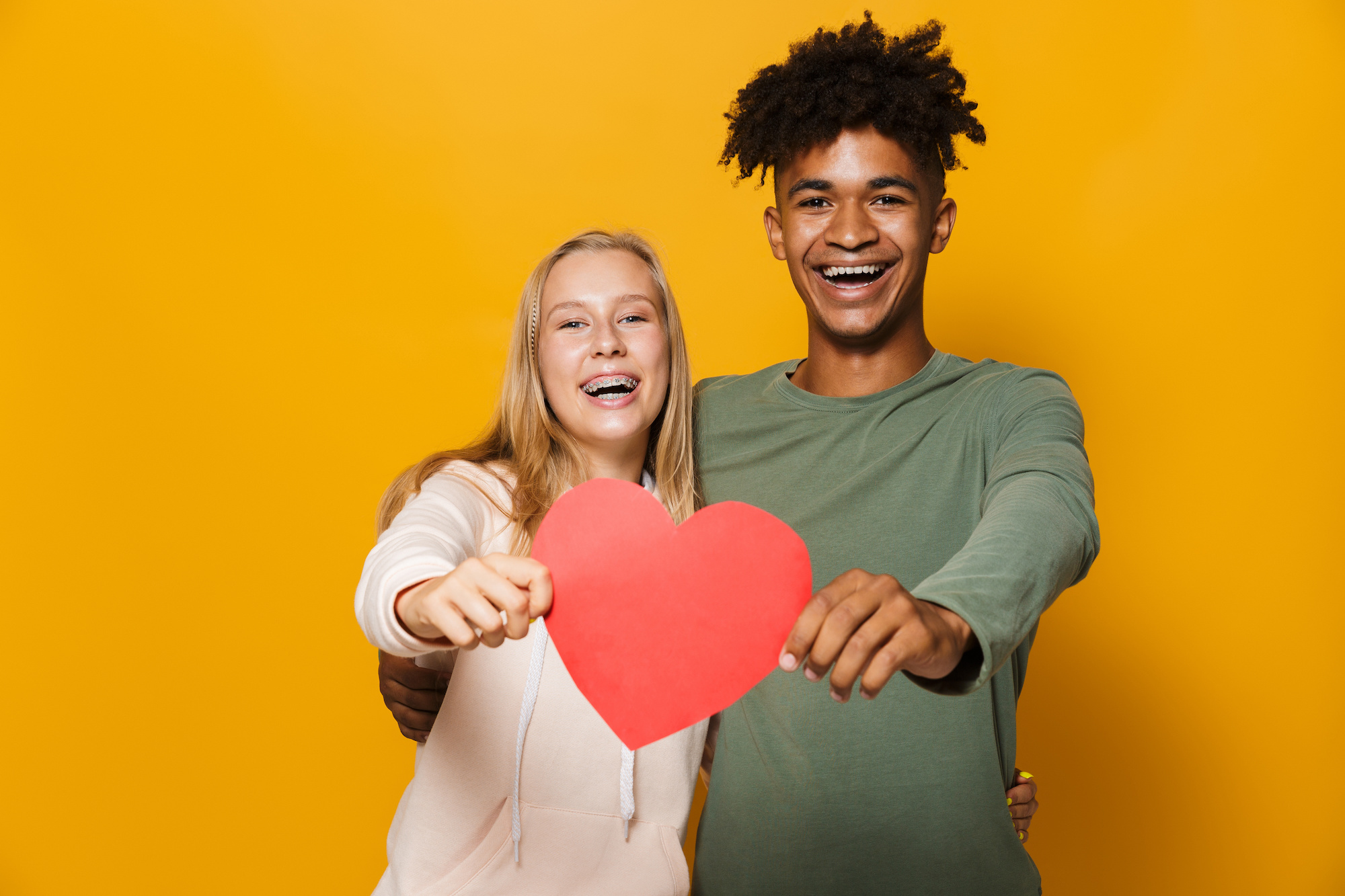 Photo of teenage friends man and woman 16-18 holding paper heart, isolated over yellow background Fairfield Orthodontics